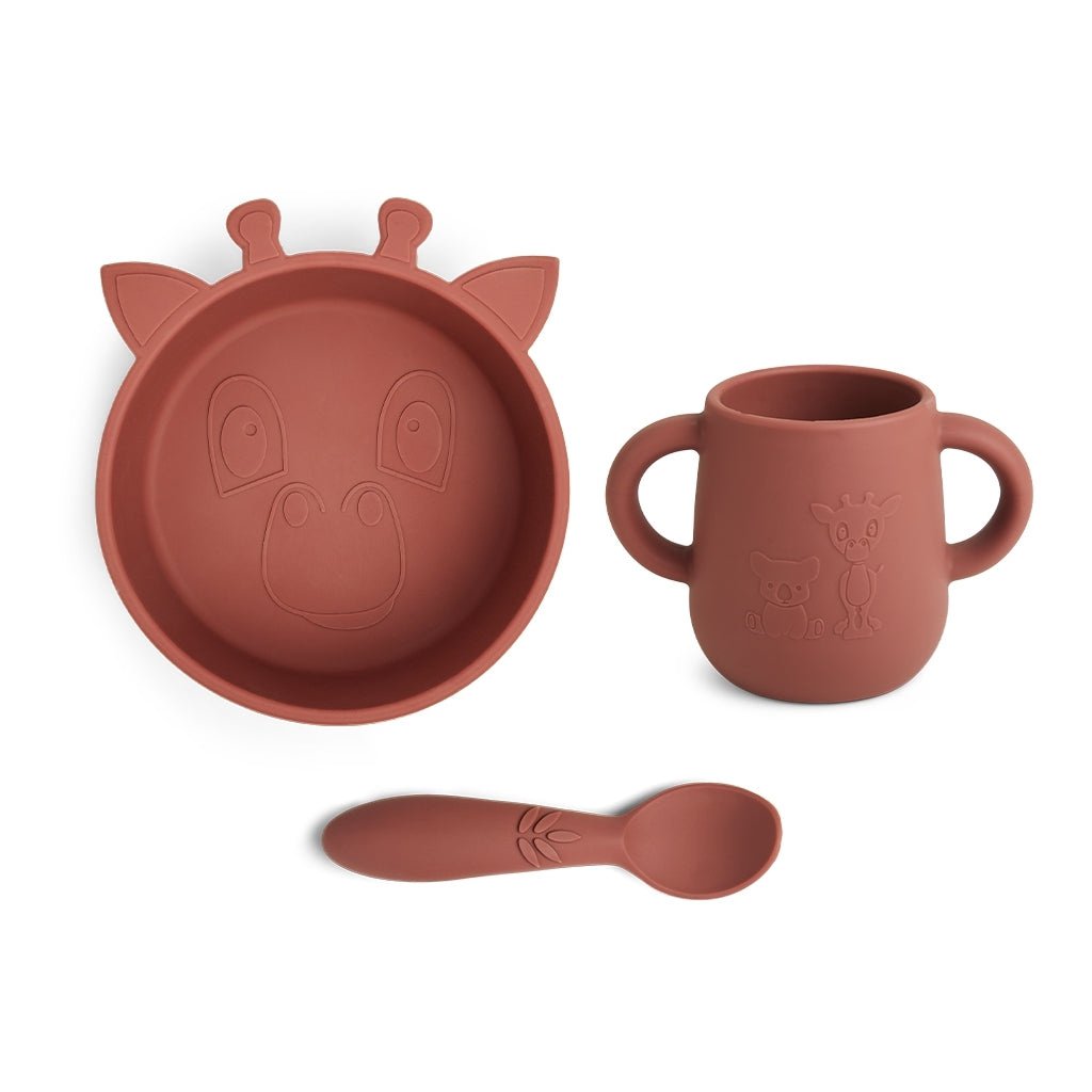 Siliconen eetset in kleur terracotta voor baby's eerste hapjes. De set bestaat uit 3 stuks: een diep bord, beker met handvat en een lepel, allemaal met een motief van een schattige giraf.